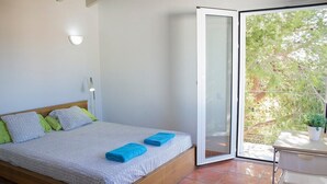 Une chambre à coucher comprenant un lit, une table de chevet, une fenêtre donnant sur des arbres et une porte coulissante.