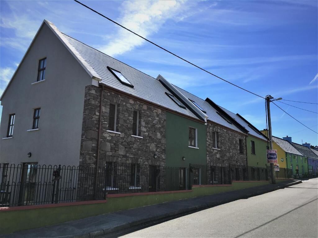 Una hilera de casas con fachada de piedra, una puerta verde y un cartel de 'For Sale'.