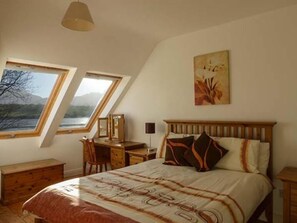 Une chambre à coucher comprenant un lit, un bureau et deux fenêtres donnant sur un paysage.