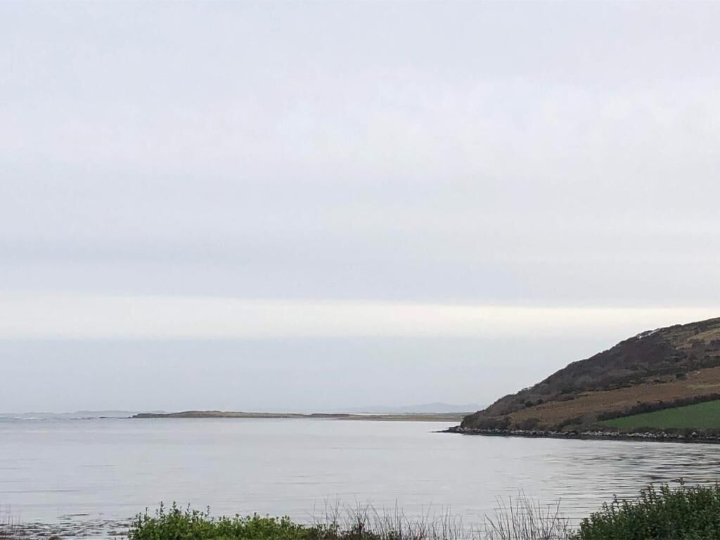 A coastal landscape with calm water, a distant shoreline, and a hilly area with sparse vegetation.
