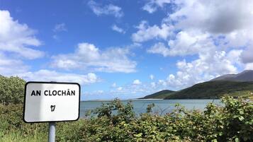 A sign with "AN CLOCHAN" written on it, surrounded by greenery and a scenic view of a lake and hills.