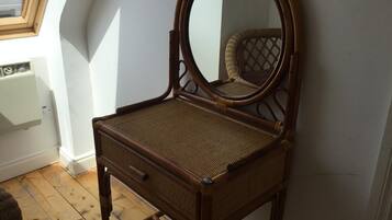 Une coiffeuse en bois avec un miroir, placée près d’une fenêtre donnant sur le ciel.