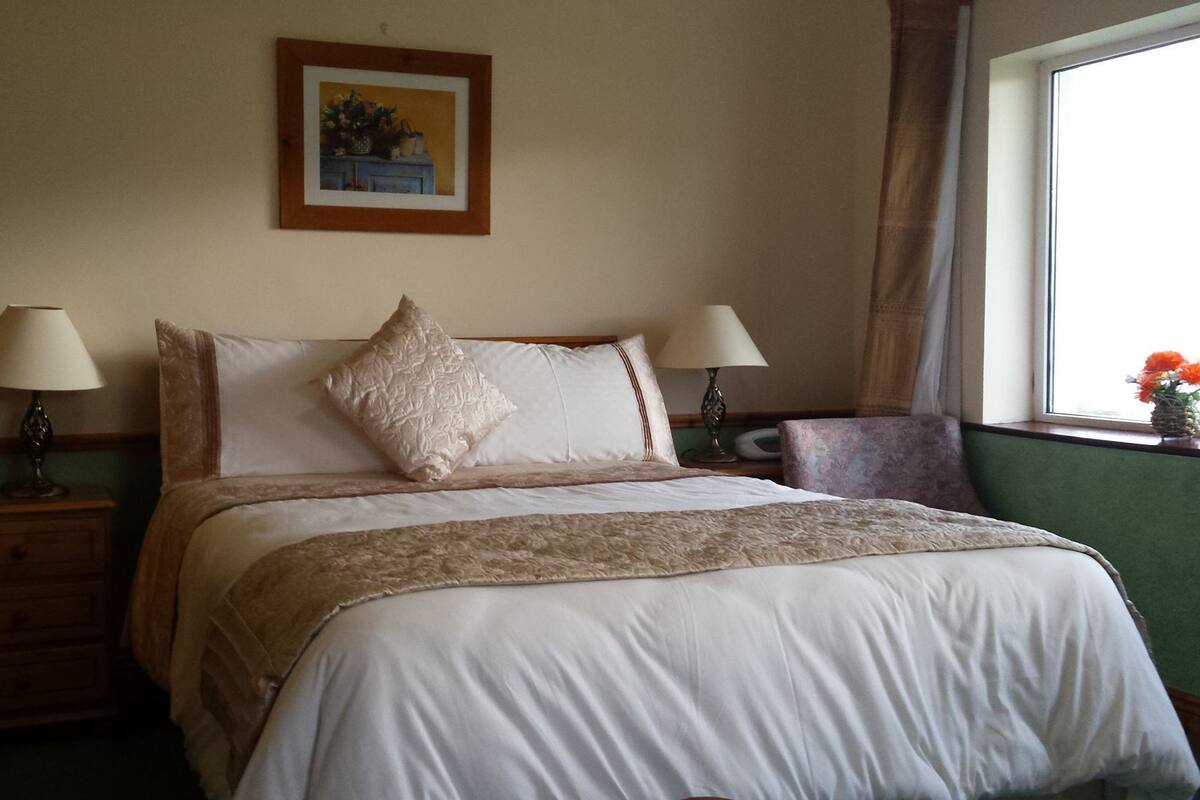 A neatly made bed with a floral bedspread, two bedside lamps, a nightstand, and a framed picture on the wall.