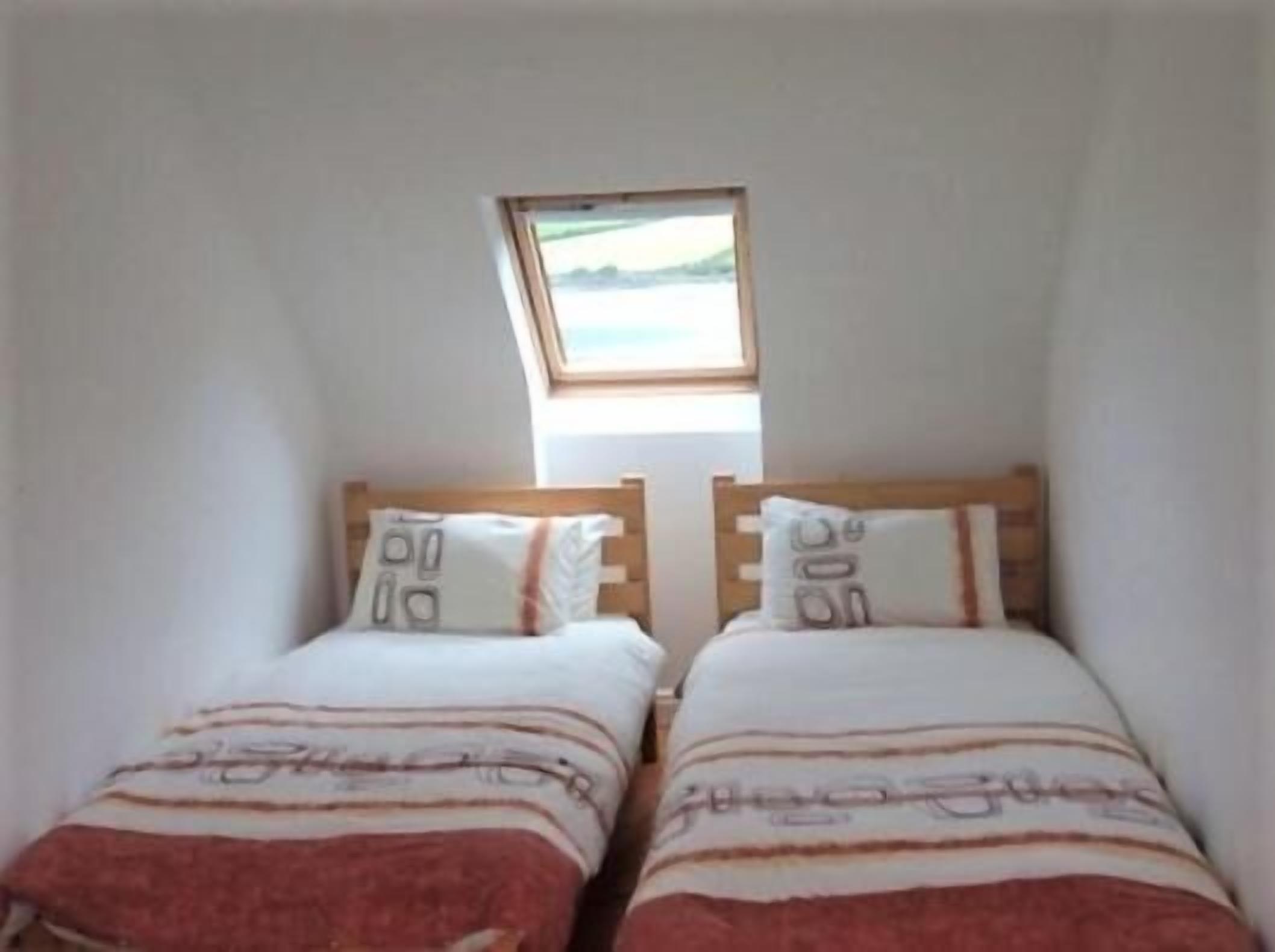 Un alojamiento pequeño y de una sola habitación con dos camas individuales, un tragaluz y vistas al exterior.