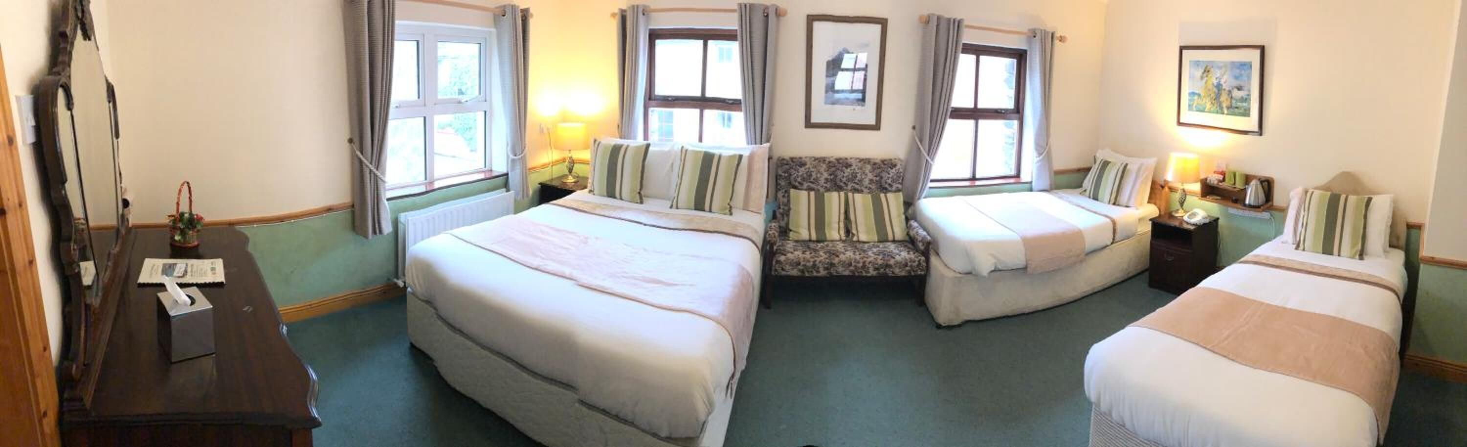 Een hotelkamer met drie bedden, een bank, een bureau en een spiegel.