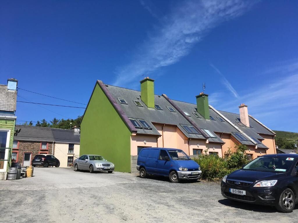 A residential area with a green house, a blue van, and a black car parked in front.