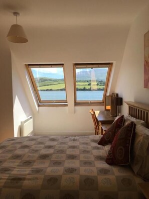 A bedroom with a large bed, two windows, a desk, and a chair. - O'Connors Guesthouse (Cloghane)