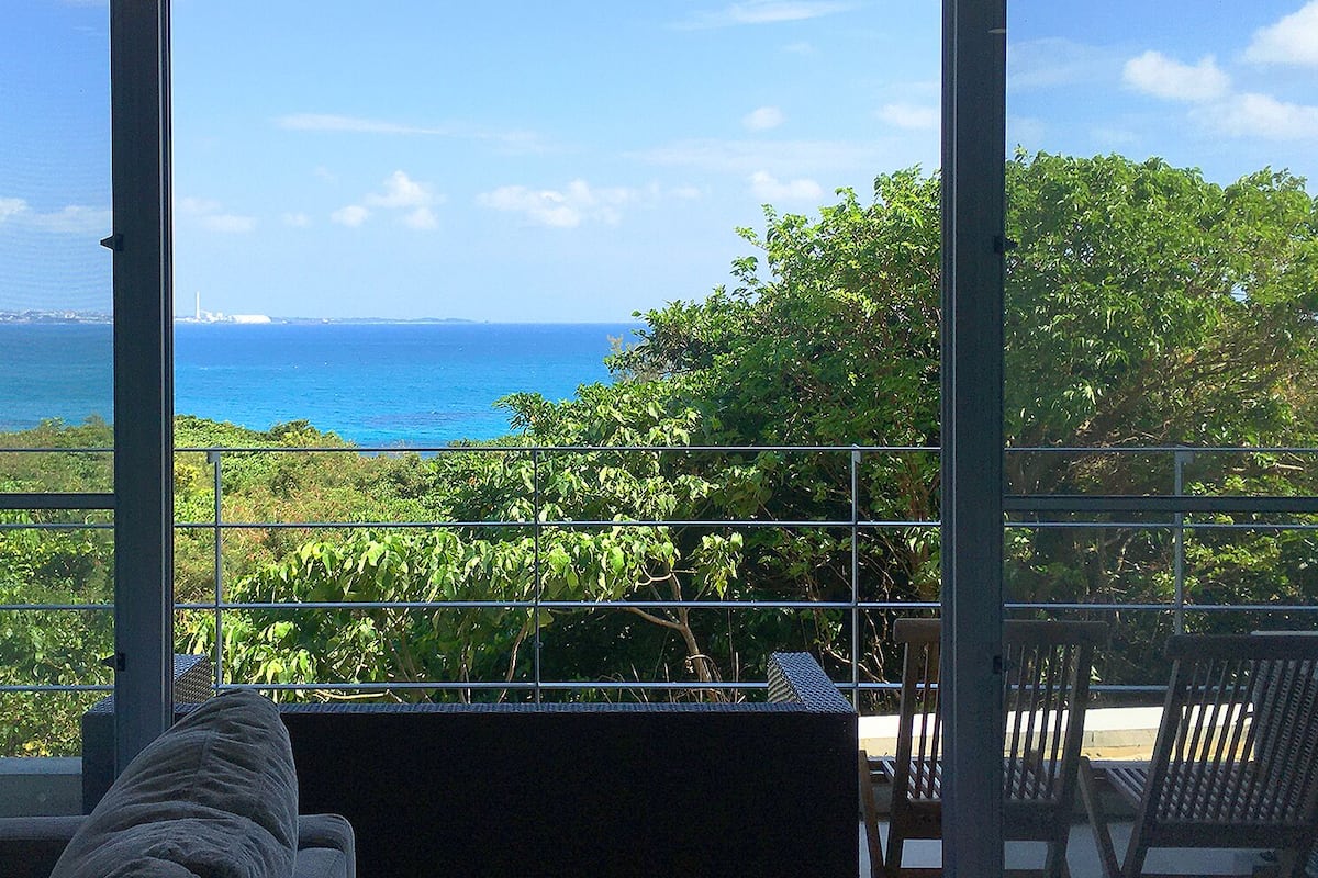 A room with a large window offering a view of the sea and distant land.