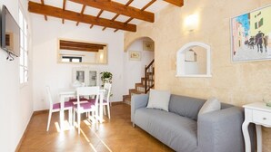 A cozy living room with a grey sofa, white chairs, a dining table, and a staircase leading to another level. - Roques 24, 3 bedroom house, Ciutadella (Ciutadella de Menorca)