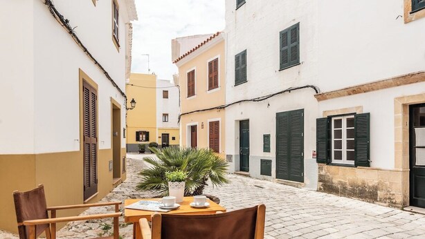 A narrow cobblestone street with a table and chairs set up for outdoor dining, surrounded by buildings with shutters and a potted plant. - Roques 24, 3 bedroom house, Ciutadella (Ciutadella de Menorca)
