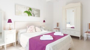 A bedroom with a large bed, white walls, a large mirror, and a painting above the bed. - Roques 24, 3 bedroom house, Ciutadella (Ciutadella de Menorca)