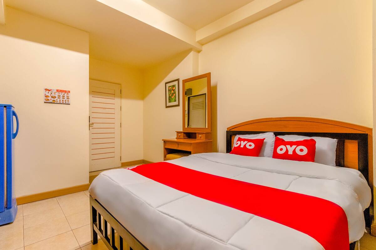 A hotel room with a bed, a desk, a mirror, and a blue chair.