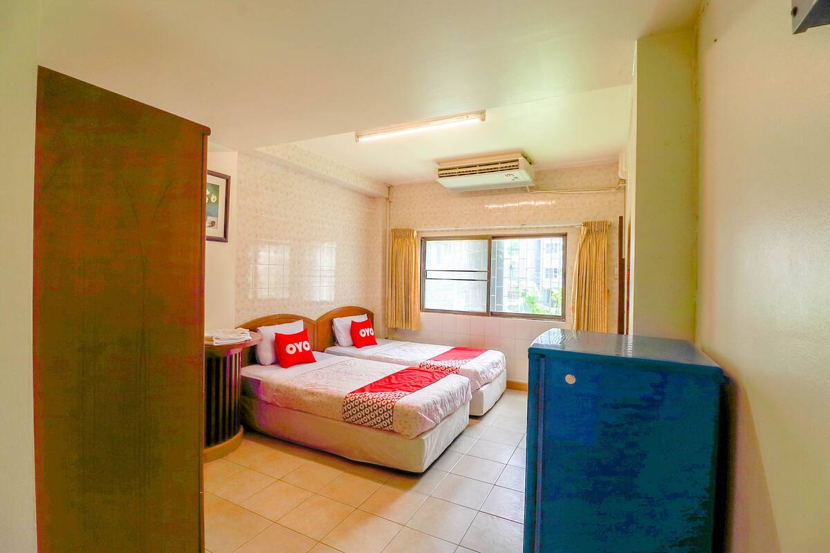 A hotel room with two beds, a radiator, a window with curtains, and a blue cabinet.