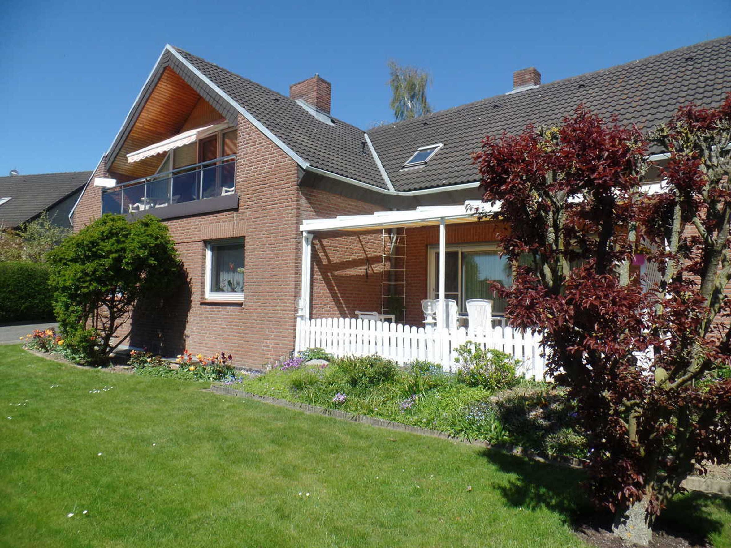 Ein zweistöckiges Haus mit Balkon, überdachter Veranda und weißem Zaun.