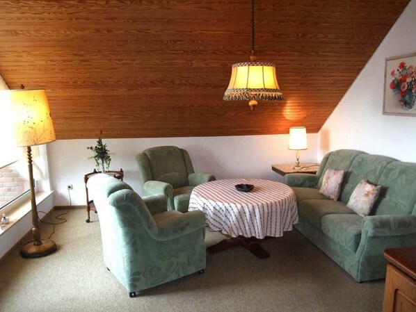 Un salon chaleureux avec un plafond en bois, une table ronde et deux fauteuils verts.