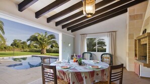 A dining area with a pool view, wooden chairs, a table with a tablecloth, and a brick fireplace.