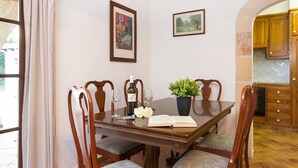 A dining room with a wooden table, chairs, a vase with flowers, a wine bottle, and two framed pictures on the wall.