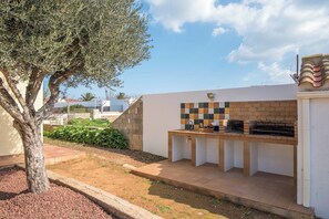 An outdoor kitchen area with a tiled backsplash, a brick oven, and a tree in the foreground.