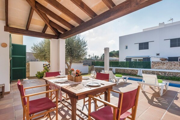 Une terrasse extérieure avec une table en bois dressée pour le repas, entourée de chaises.