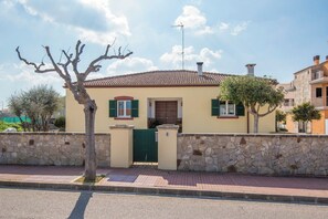 Une maison de plain-pied avec un toit en tuiles, un mur en pierre et un portail vert.