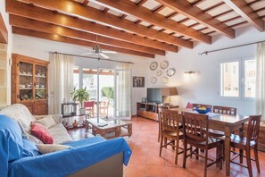 Un'ampia zona giorno con soffitto in legno, un divano, un tavolo da pranzo con sedie e una televisione.