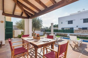 Patio esterno con tavolo in legno apparecchiato per mangiare, circondato da sedie.