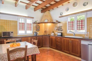 A kitchen with wooden cabinets, a tiled backsplash, a dining table with chairs, and a clock on the wall.