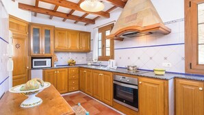 A kitchen with wooden cabinets, a microwave, an oven, and a stone chimney. - Sa Font 45, 4 bedroom house, Ciutadella (Ciutadella de Menorca)