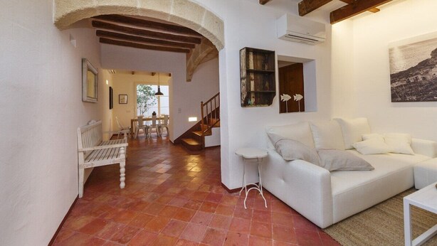 A spacious living area with a white sofa, a small table, and a bench. There is a staircase leading to another room, and a large window with a view. - Sant Isidre 50, 4 bedroom house, Ciutadella (Ciutadella de Menorca)