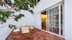 A patio with a wooden table and chairs, a white wall, and a sliding glass door leading to an interior space. - Sant Isidre 50, 4 bedroom house, Ciutadella (Ciutadella de Menorca)