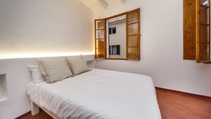A bedroom with a bed, a wooden-framed mirror, and a window with wooden shutters. - Sant Isidre 50, 4 bedroom house, Ciutadella (Ciutadella de Menorca)