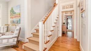 A staircase with wooden steps and white railings, leading to a hallway with a view of the outside. - Updated Wilson Village 4 Bedroom Cottage  Amenity access available (Bluffton)