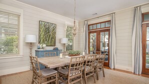 A dining room with a wooden table and chairs, a chandelier, and a large window with blinds. - Updated Wilson Village 4 Bedroom Cottage  Amenity access available (Bluffton)