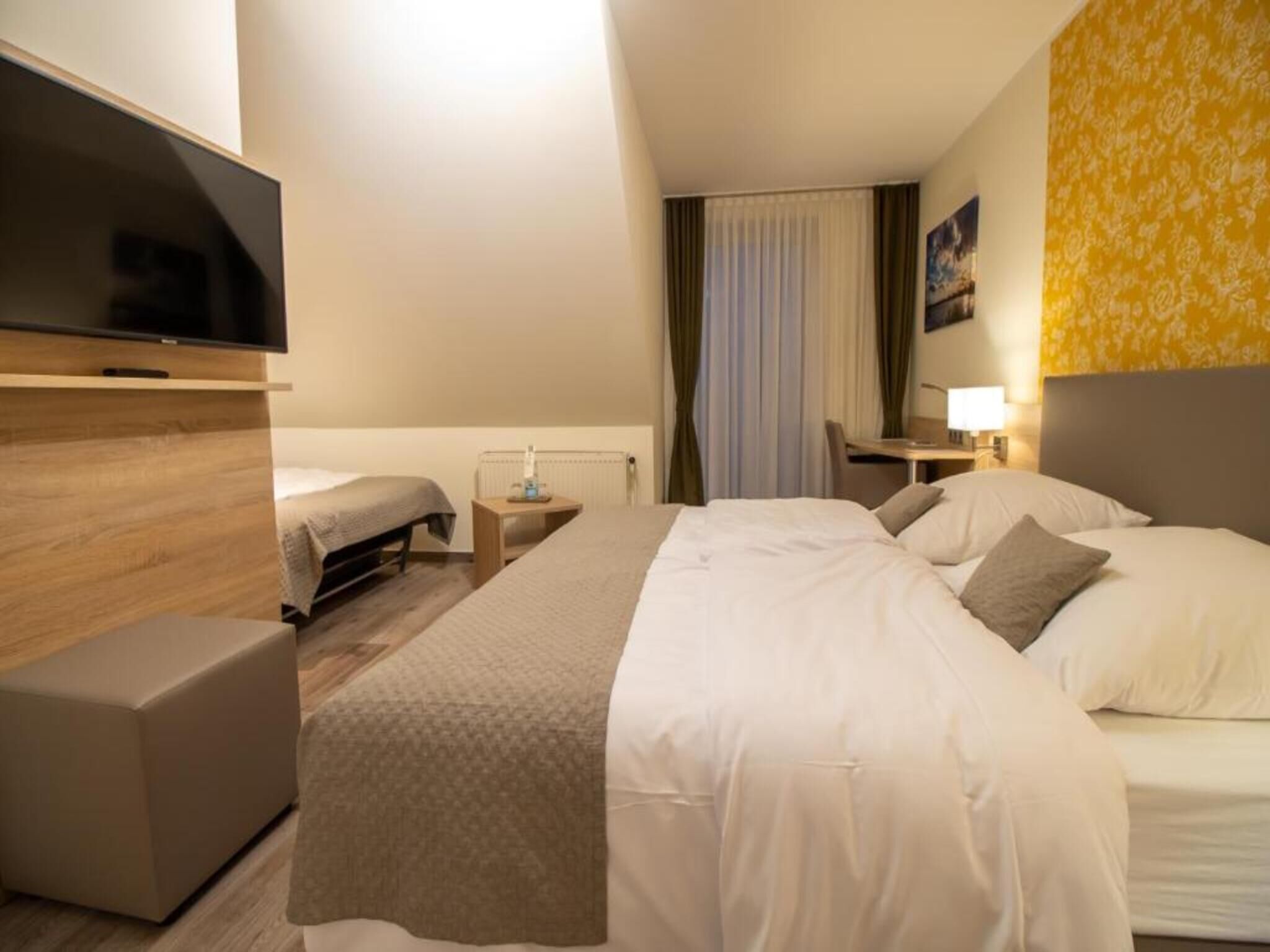 Une chambre d’hôtel avec un lit, un bureau, une télévision et une fenêtre avec des rideaux.