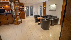 Et hotellobby med en receptionsdisk, et opholdsområde med en sofa og stole, samt en informationsplakat på væggen.