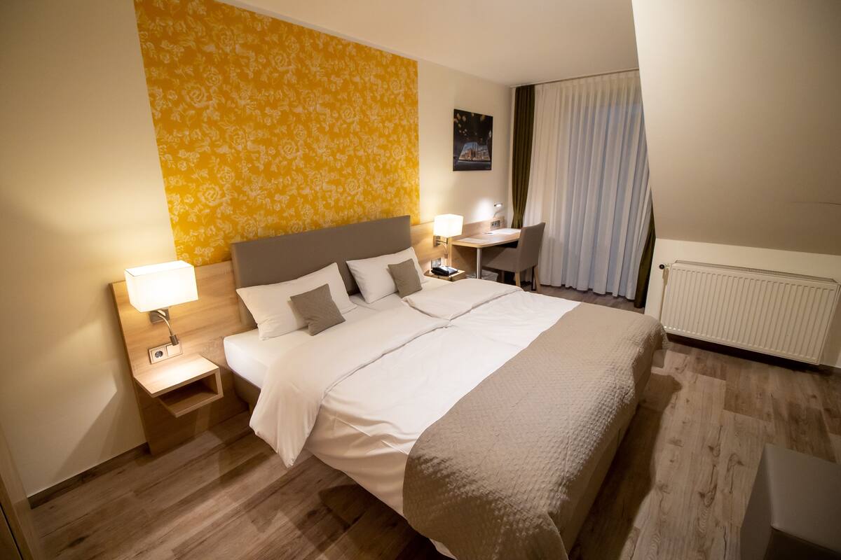 Ett hotellrum med en stor säng, sängbord med lampor, ett skrivbord och en stol.