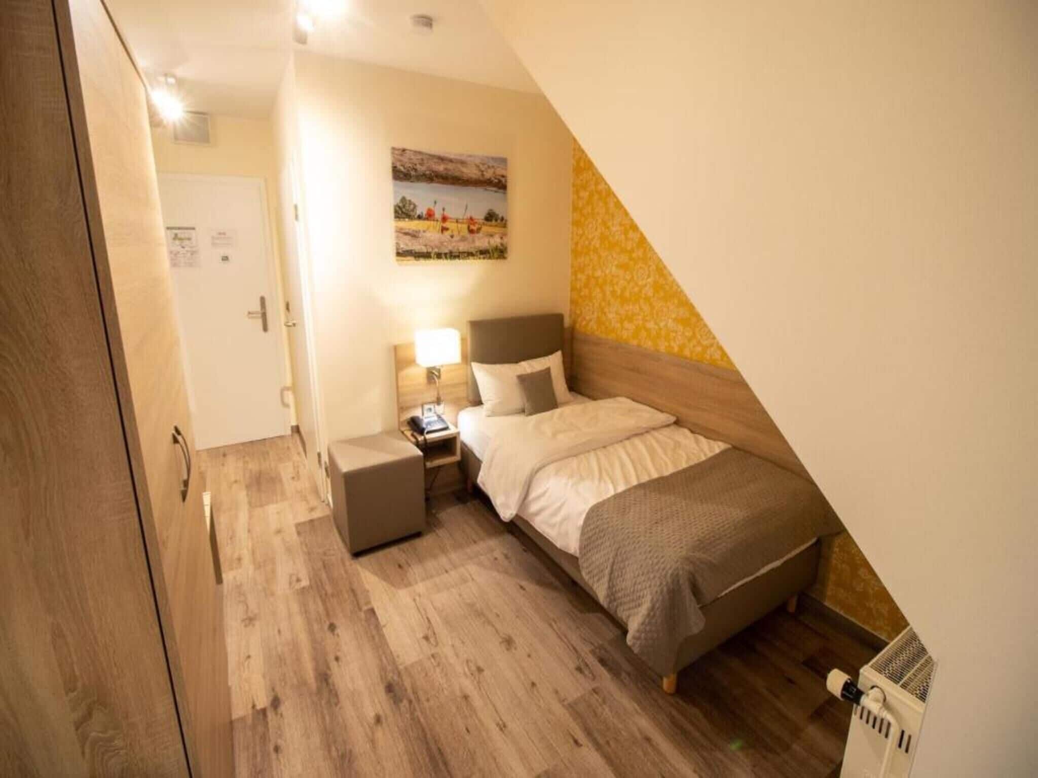 A bedroom with a bed, bedside table, lamp, and a painting on the wall.