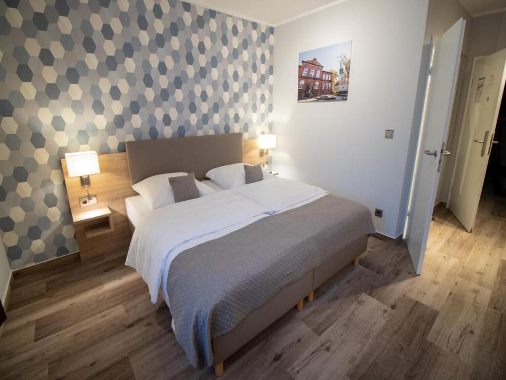 Una camera da letto con un letto, due comodini con lampade, una testiera in legno, una parete decorata e una porta.