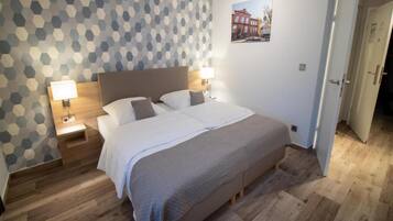 Una camera da letto con un letto, due comodini con lampade, una testiera in legno, una parete decorata e una porta.