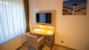 Et hotelværelse med skrivebord, stol, TV og et skilt på væggen med information om vejen.