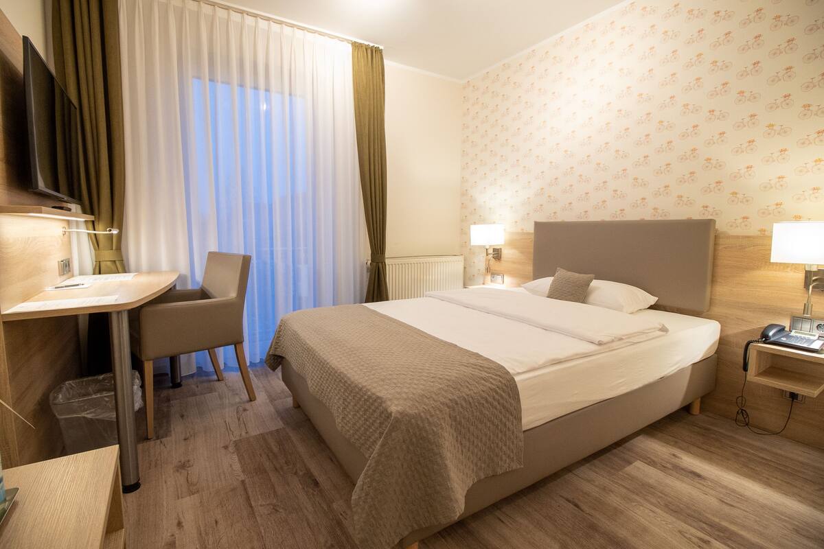 Ett hotellrum med en säng, ett skrivbord, en stol, en tv och en lampa.