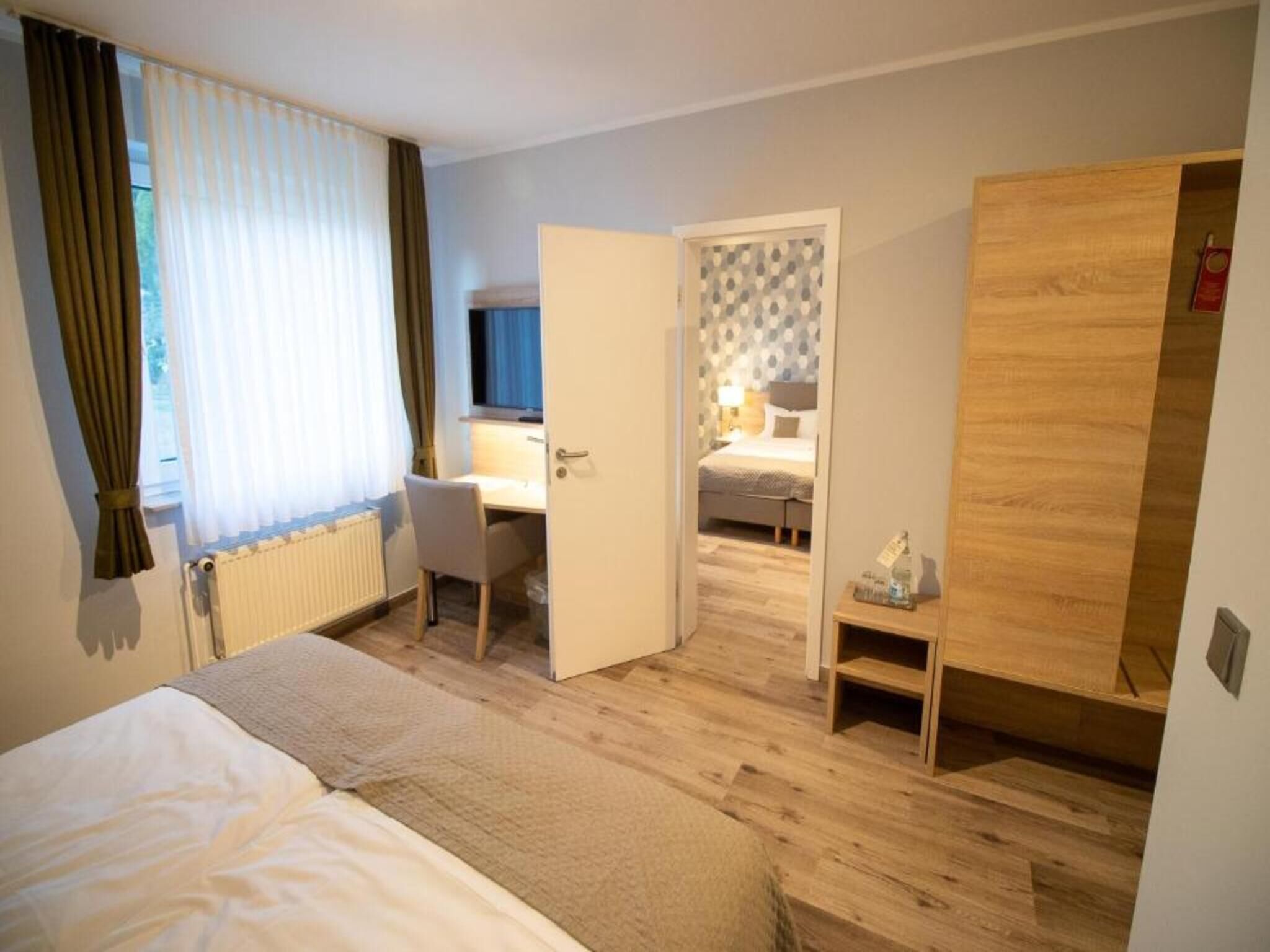 A hotel room with a bed, a desk, a chair, and a wardrobe.