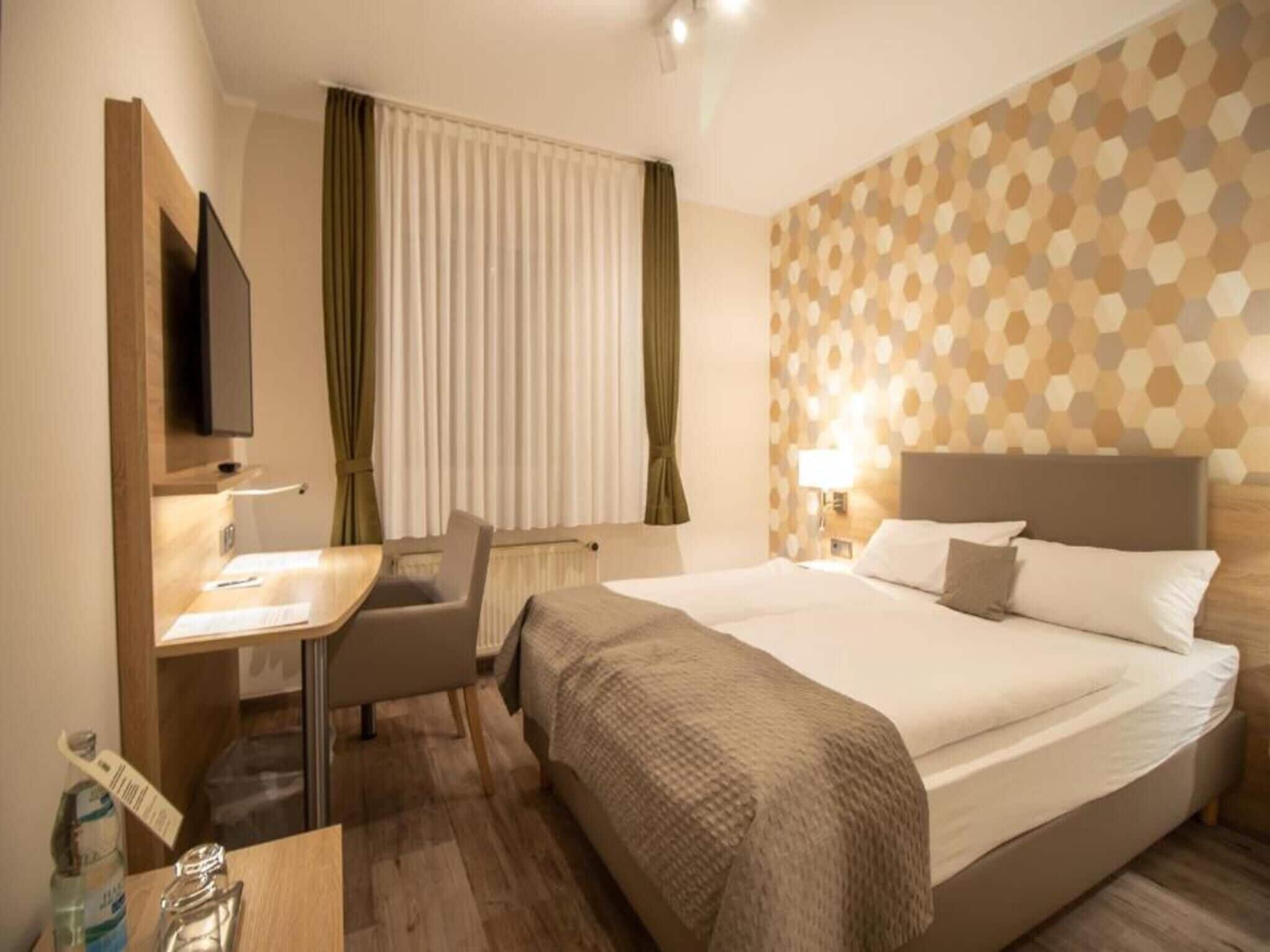 A hotel room with a bed, a desk, a chair, a television, and a window with curtains.