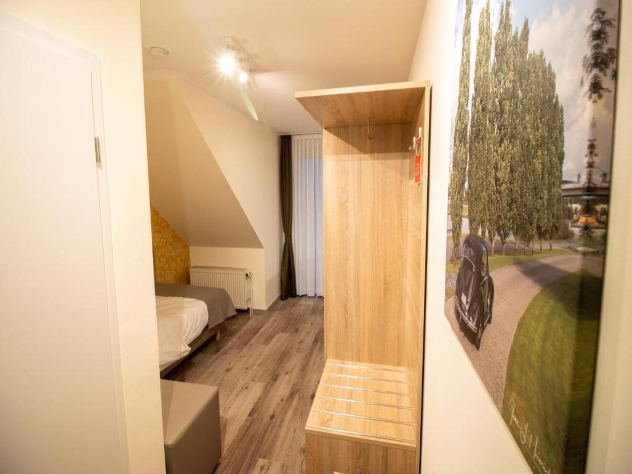 A bedroom with a bed, a radiator, a wooden wardrobe, and a painting of trees.