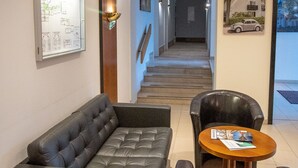Et hotel lobby med sofa, stole, et bord, et indrammet kort og en trappe.