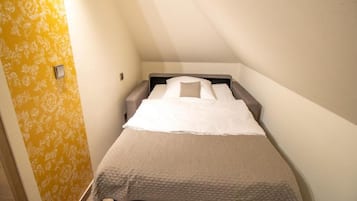 A small, single-bed room with a plain bed, a nightstand, and a wall-mounted light.