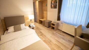 Ein Hotelzimmer mit Bett, Nachttisch, Lampe, einer kleinen Holzbank, einem Sessel und einem Heizkörper.