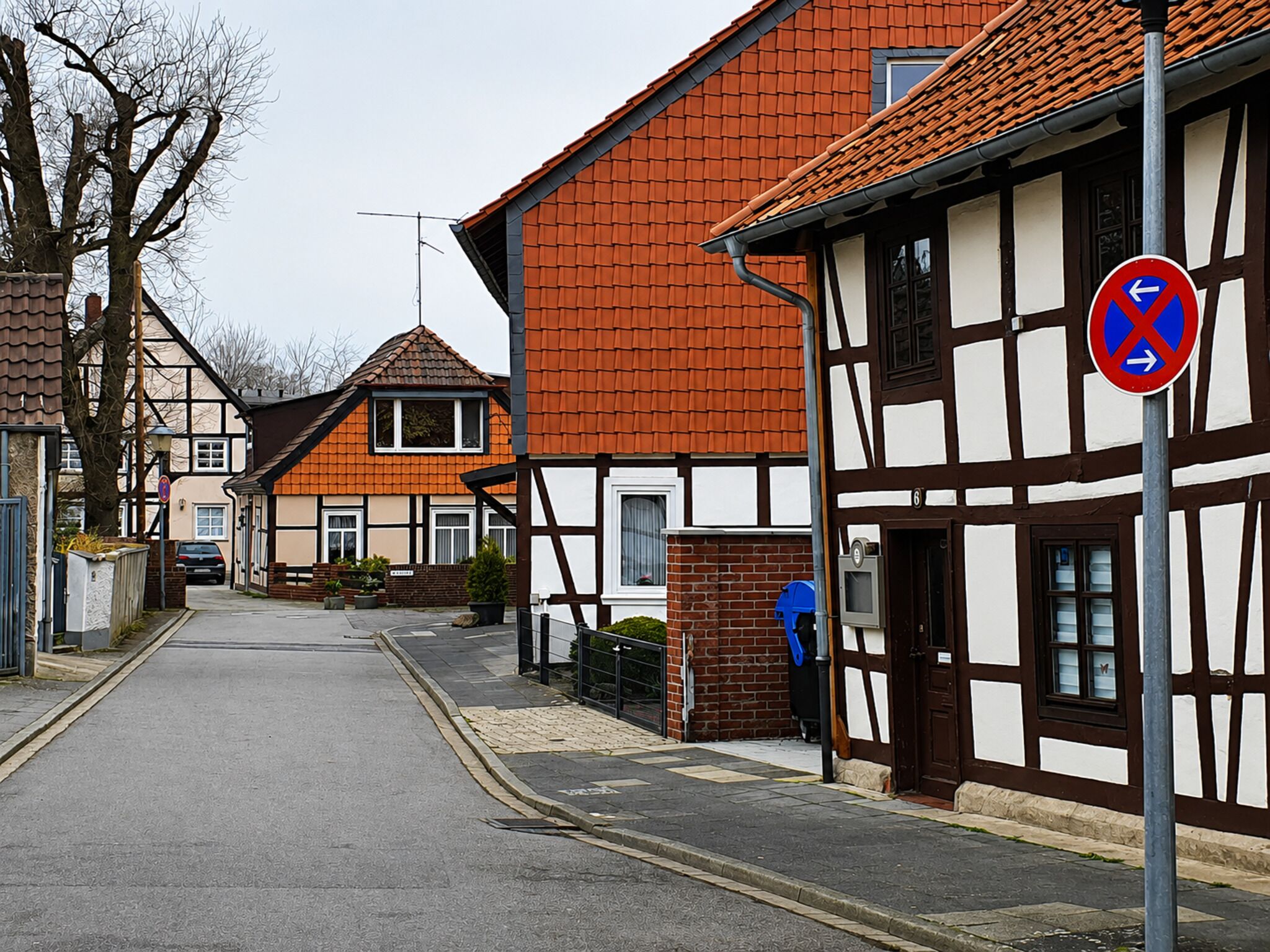 Una calle estrecha flanqueada por casas tradicionales de entramado de madera, una señal de prohibido estacionar y un buzón.