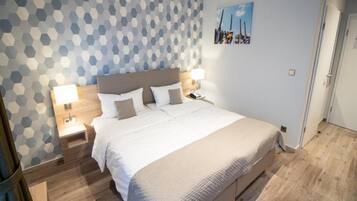 Una habitación de hotel con una cama grande, suelo de madera y un papel tapiz con un motivo geométrico.