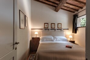 Une chambre à coucher avec un lit, deux tables de chevet avec des lampes, une porte et une fenêtre avec un rideau.